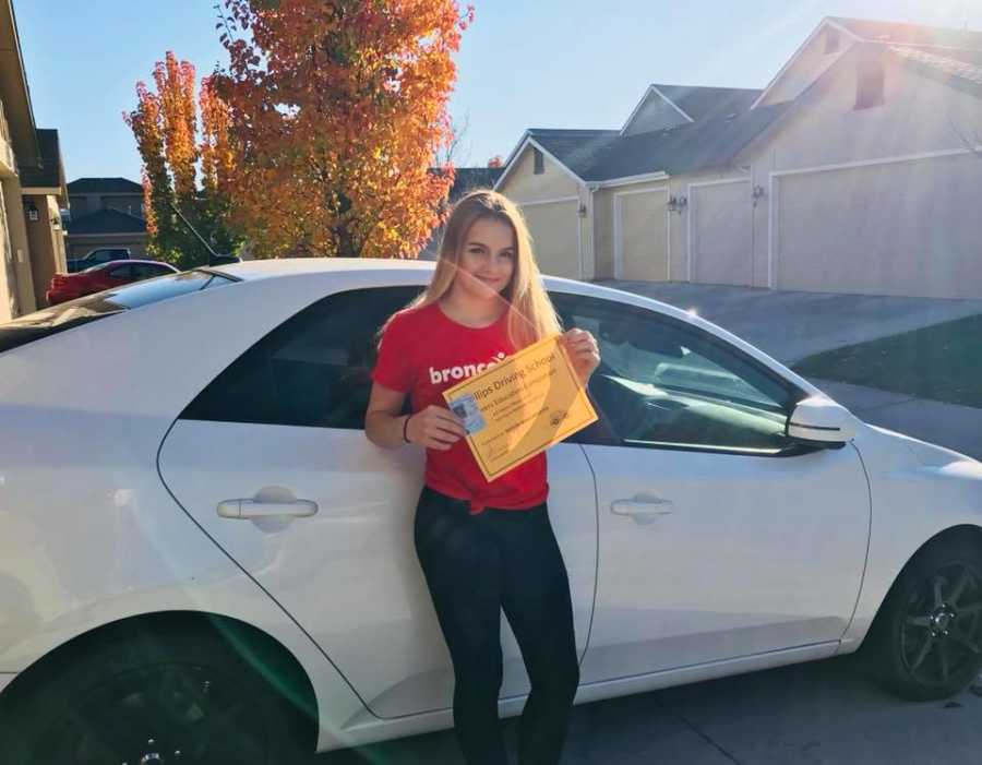 Teen stands in front of car holding driving certificate