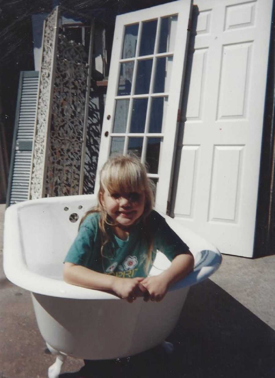 Little girl smiles as she sits in bath tub outside