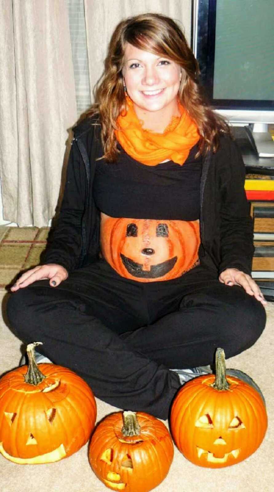 Teen mom with painted pumpkin on pregnant belly