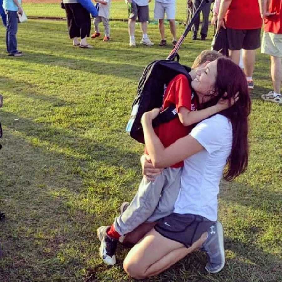 Mom hugging son on field in black backpack