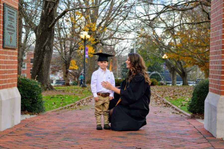 Young mom wearing college cap and gown holding son 