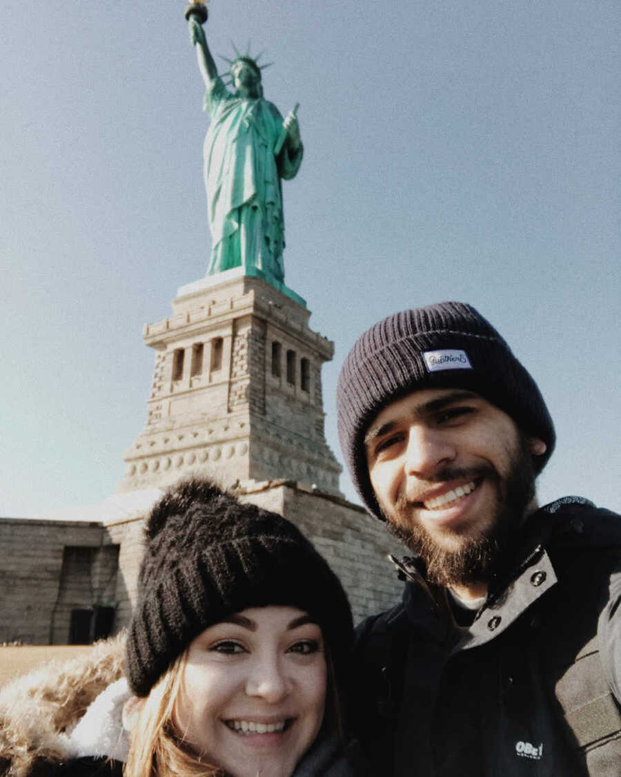 Boyfriend and girlfriend smiling in front of statue of liberty