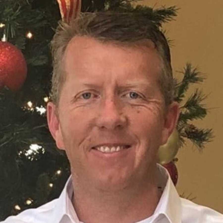 Paramedic smiling in front of decorated Christmas tree