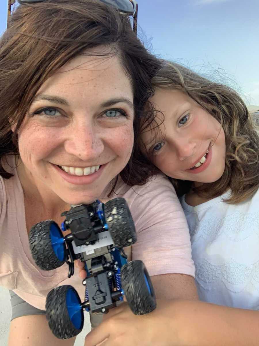 Foster mom smiling next to daughter while holding toy truck