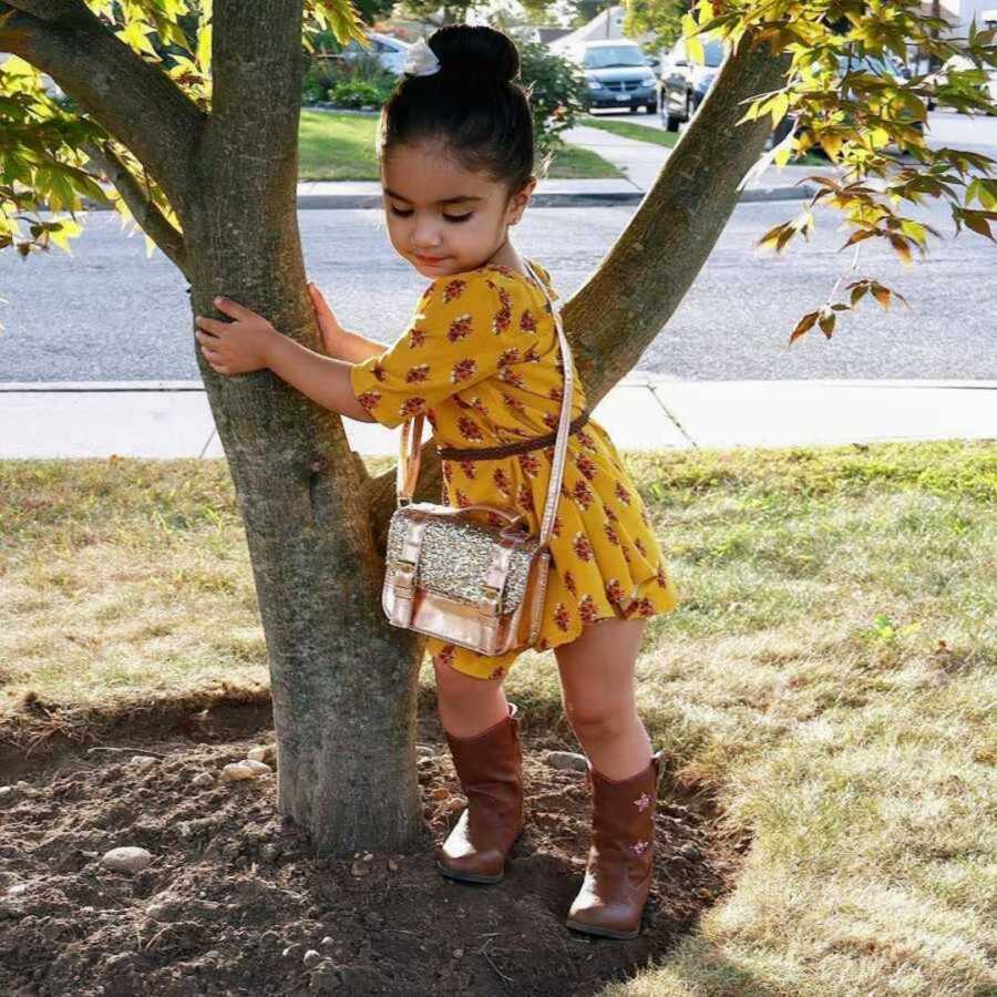 girl in yellow dress stands by tree