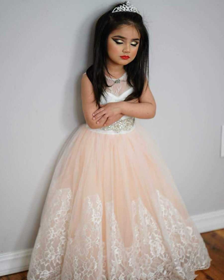 young girl stands in pink dress and full face of makeup