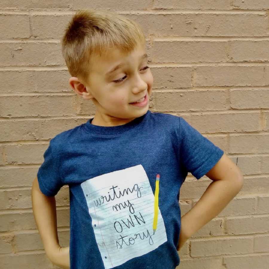 young boy smiles looking sideways and placing hands on hips