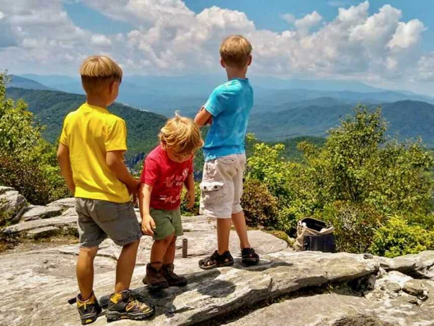 Three little boys standing on top of rock overlooking mountains