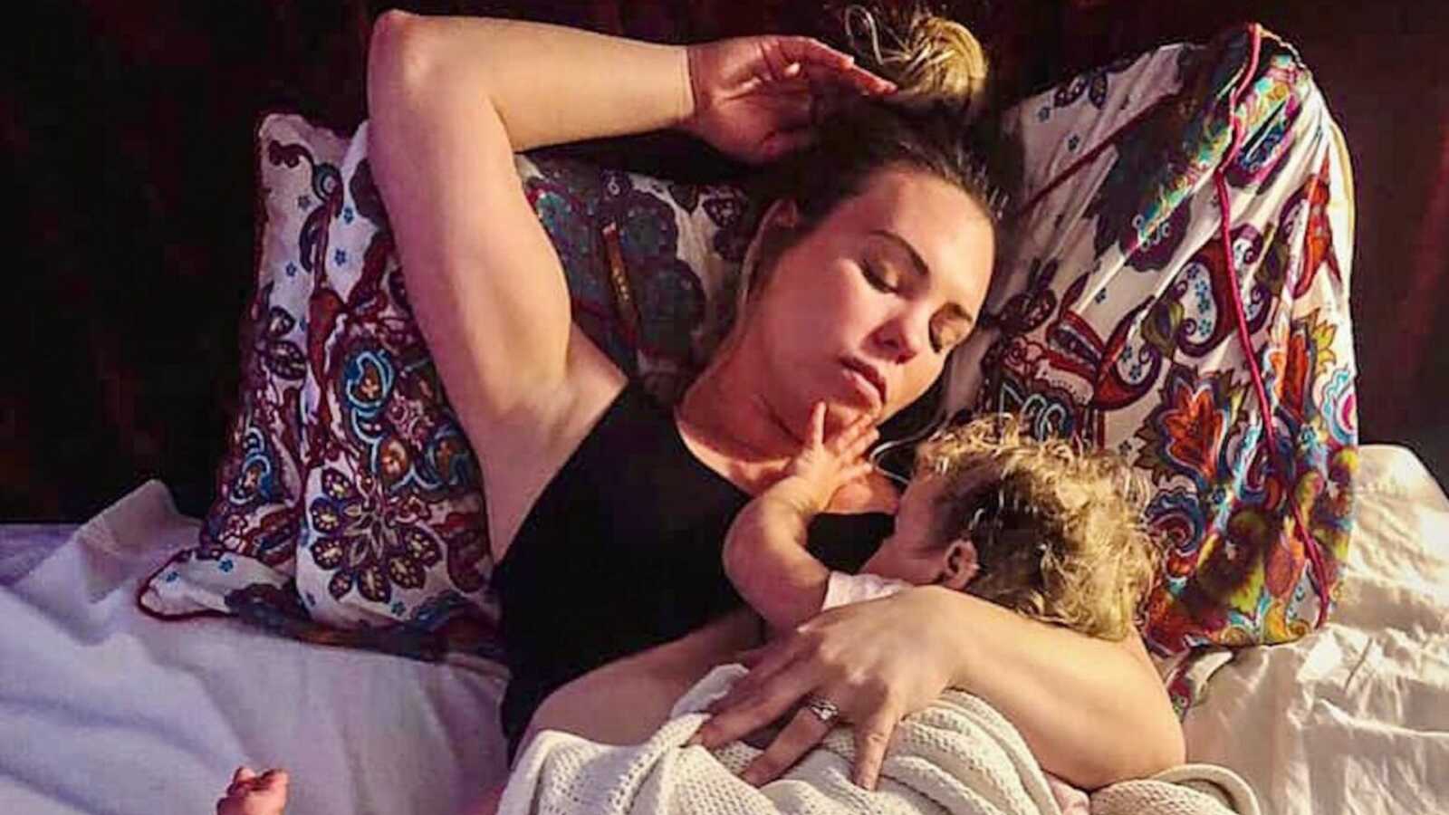 tired mom holds sleeping baby in bed