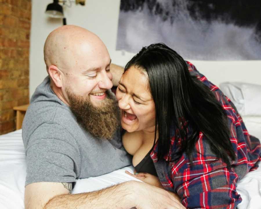domestic abuse survivor embracing with husband on bed in red and blue flannel while laughing