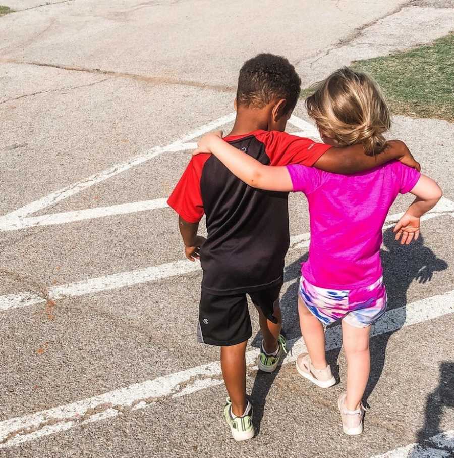 Young foster brother and sister walk together with their arms wrapped around each other's shoulders.