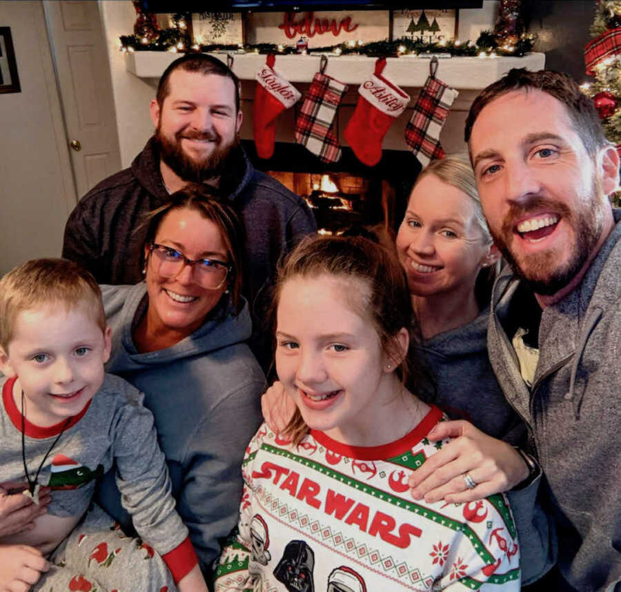 Blended family smiling beside Christmas stockings and fireplace