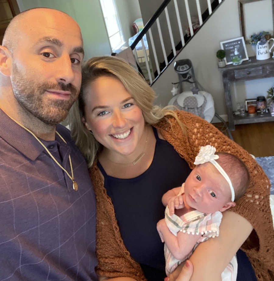 Husband and wife take picture with new baby girl in their home.