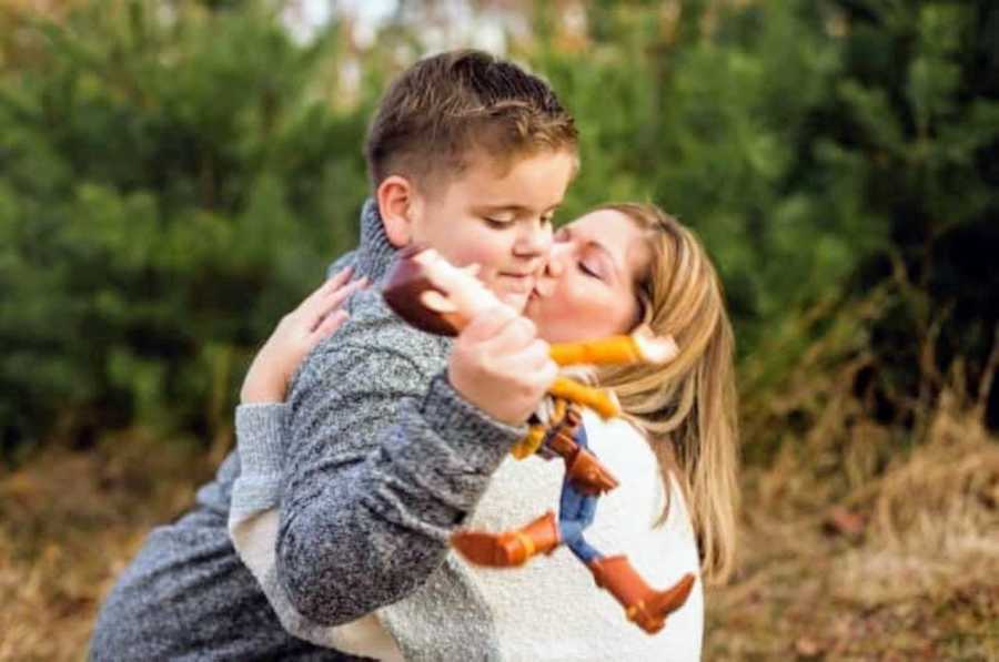 Special needs mom kisses son with autism holding Toy Story's Woody doll on cheek