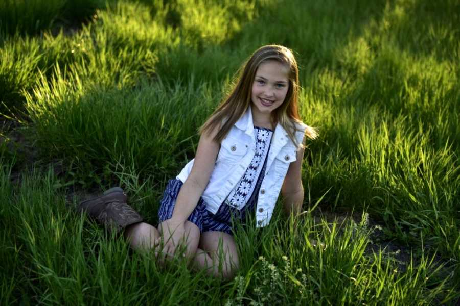 Girl with cowboy boots and white denim vest smiles in grass