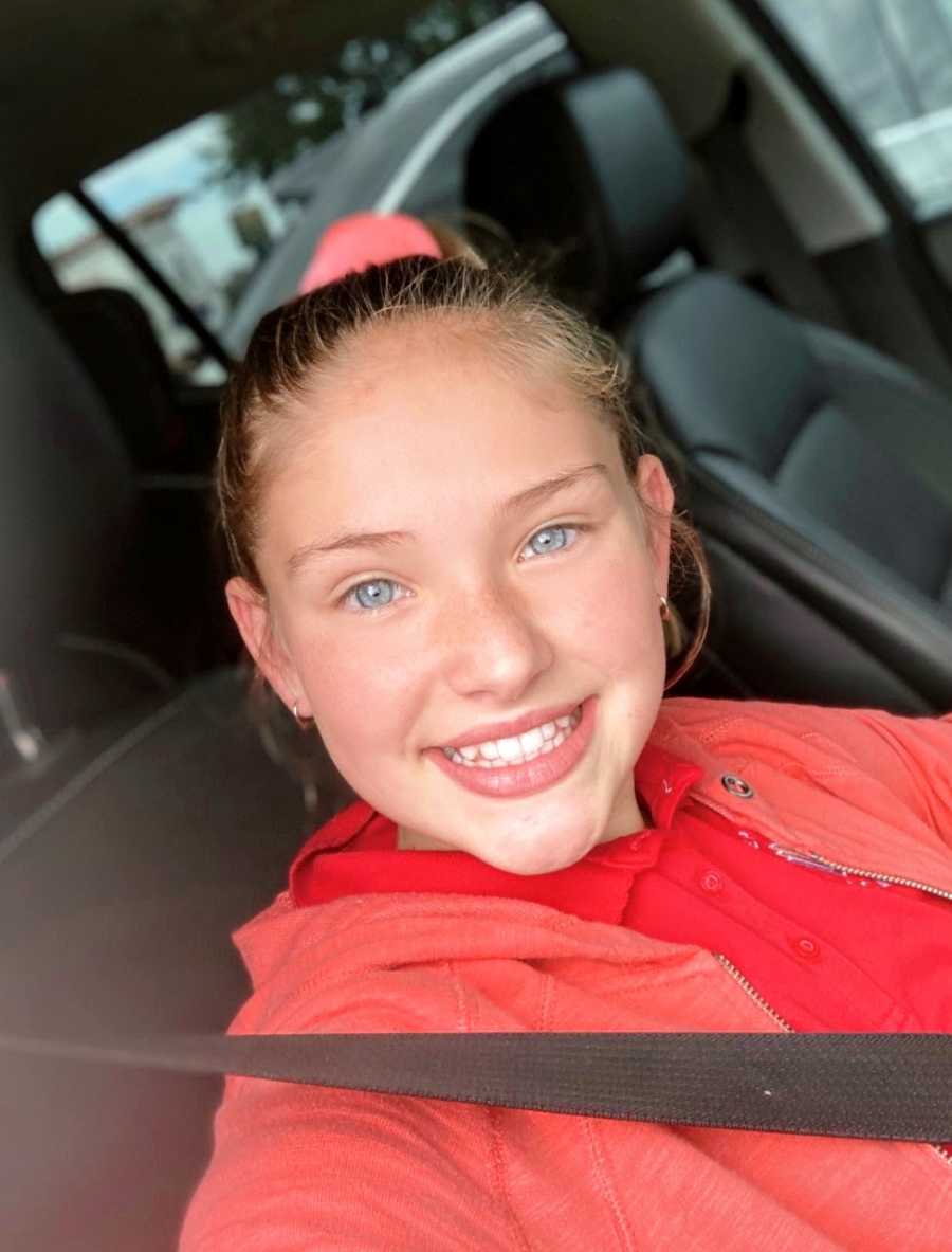 Girl with red shirt and sweater smiles for car selfie
