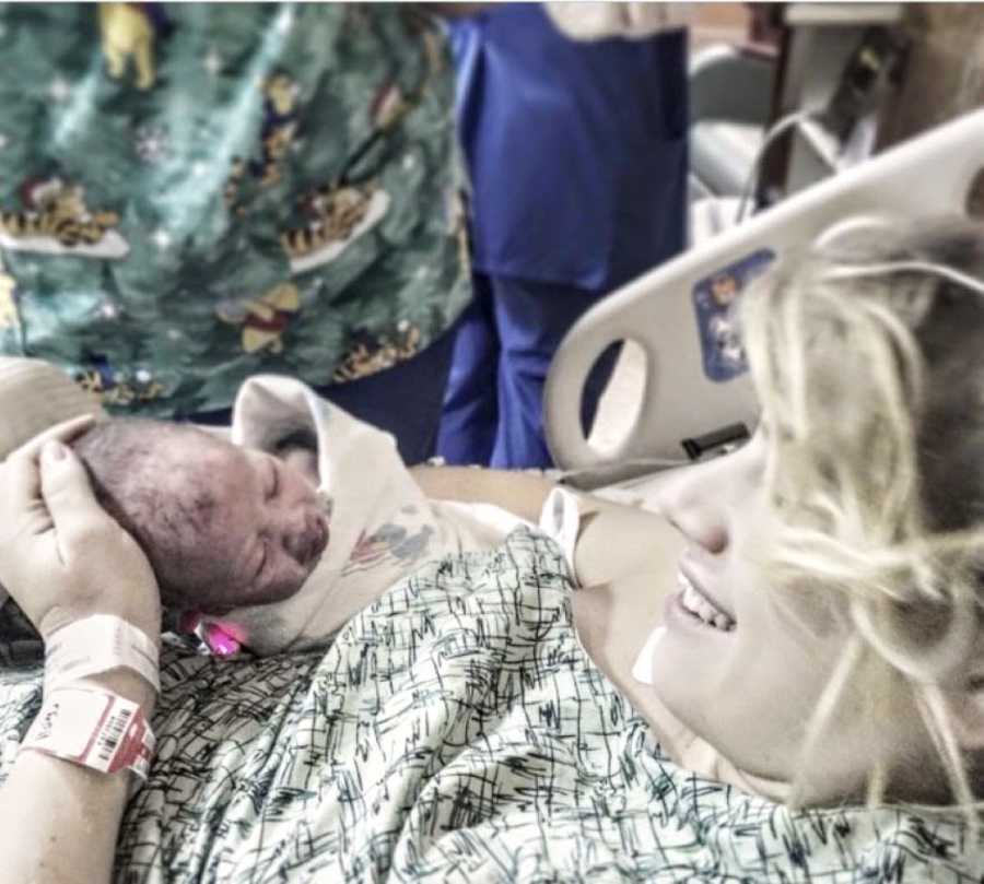 Teen mom in hospital gown holds newborn baby