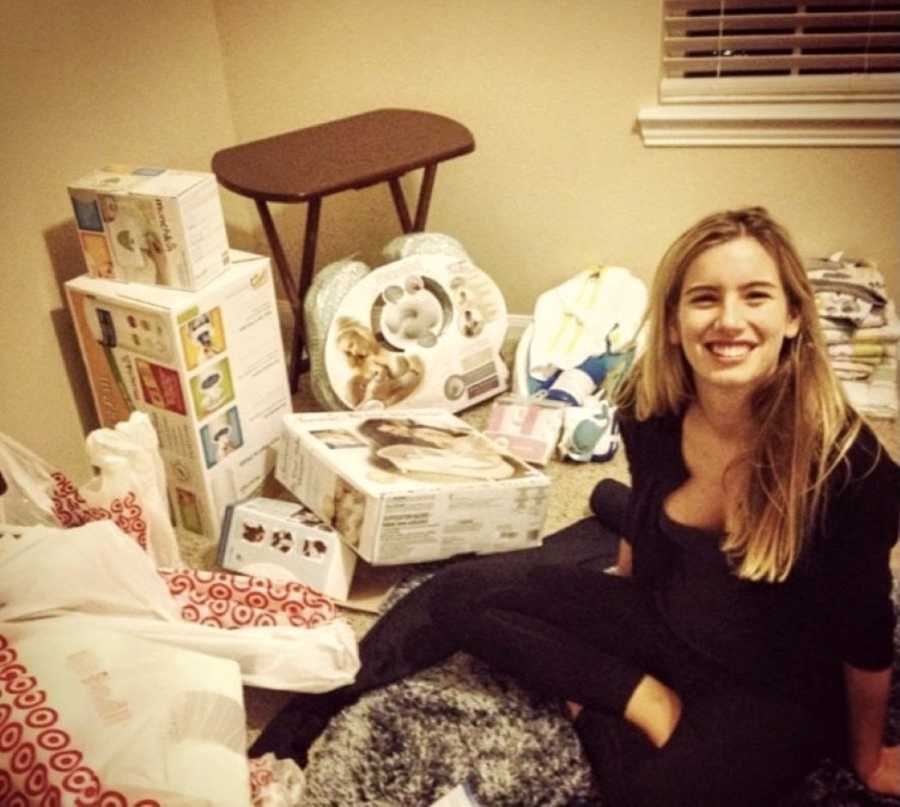 Teen mom in black shirt sits in between baby shower gifts on floor