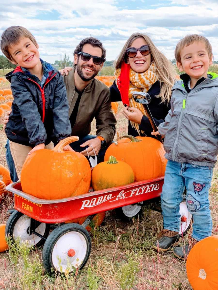 Teen mom with two sons and husband smile at pumpkin patch