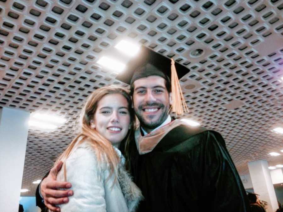 Man in black graduation cap and gown embraces girlfriend