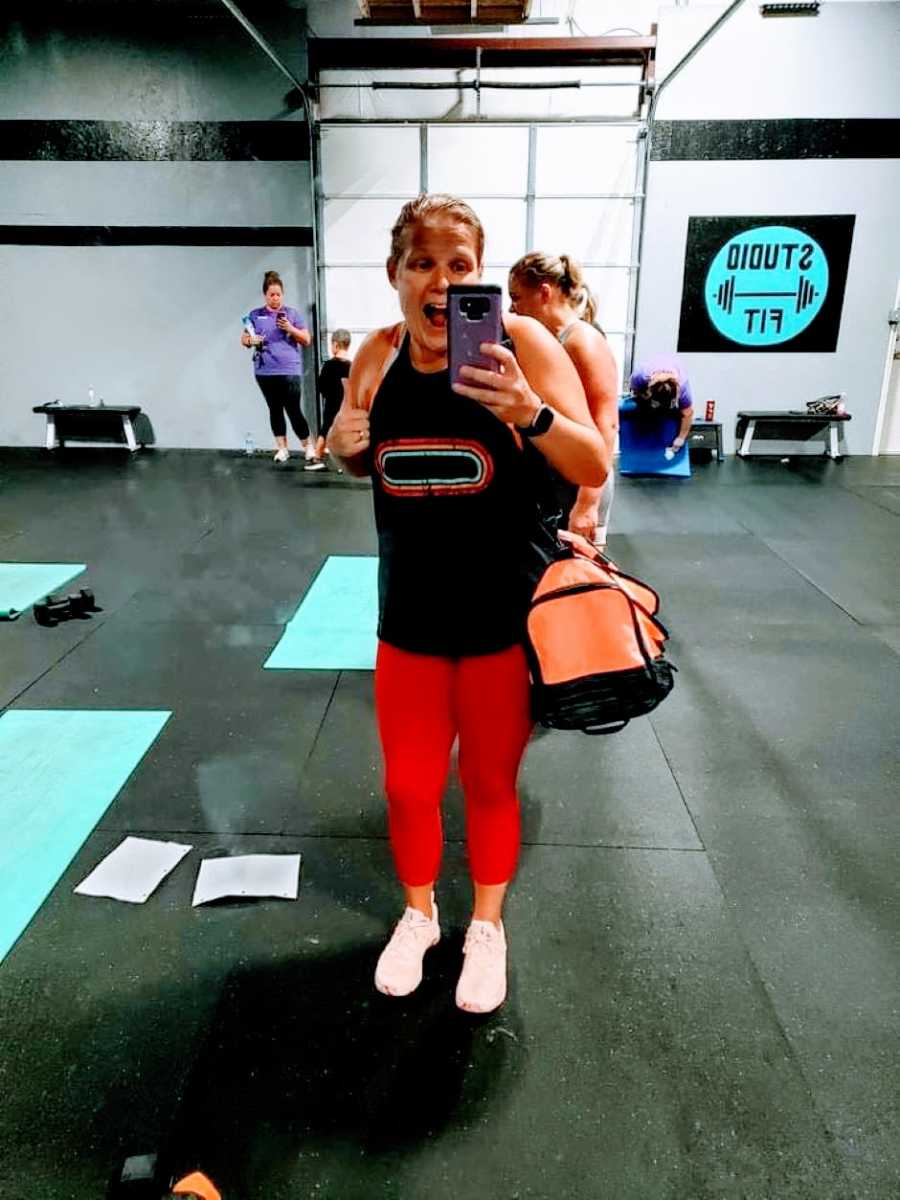 Woman in red leggings smiles big at the gym in front of mirror