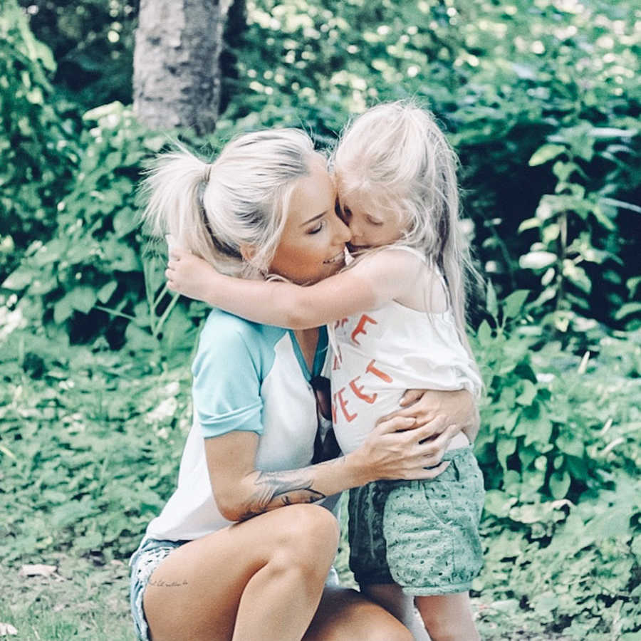 Teen mom with tattoos embraces daughter in green shorts