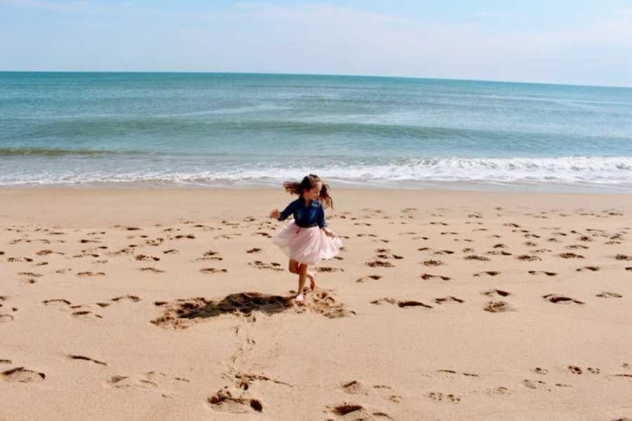 young girl twirls in the sand at the beach