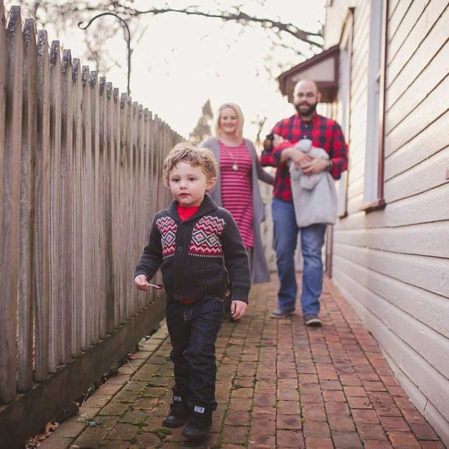 Special needs parents in red stand behind special needs son in red and grey sweater