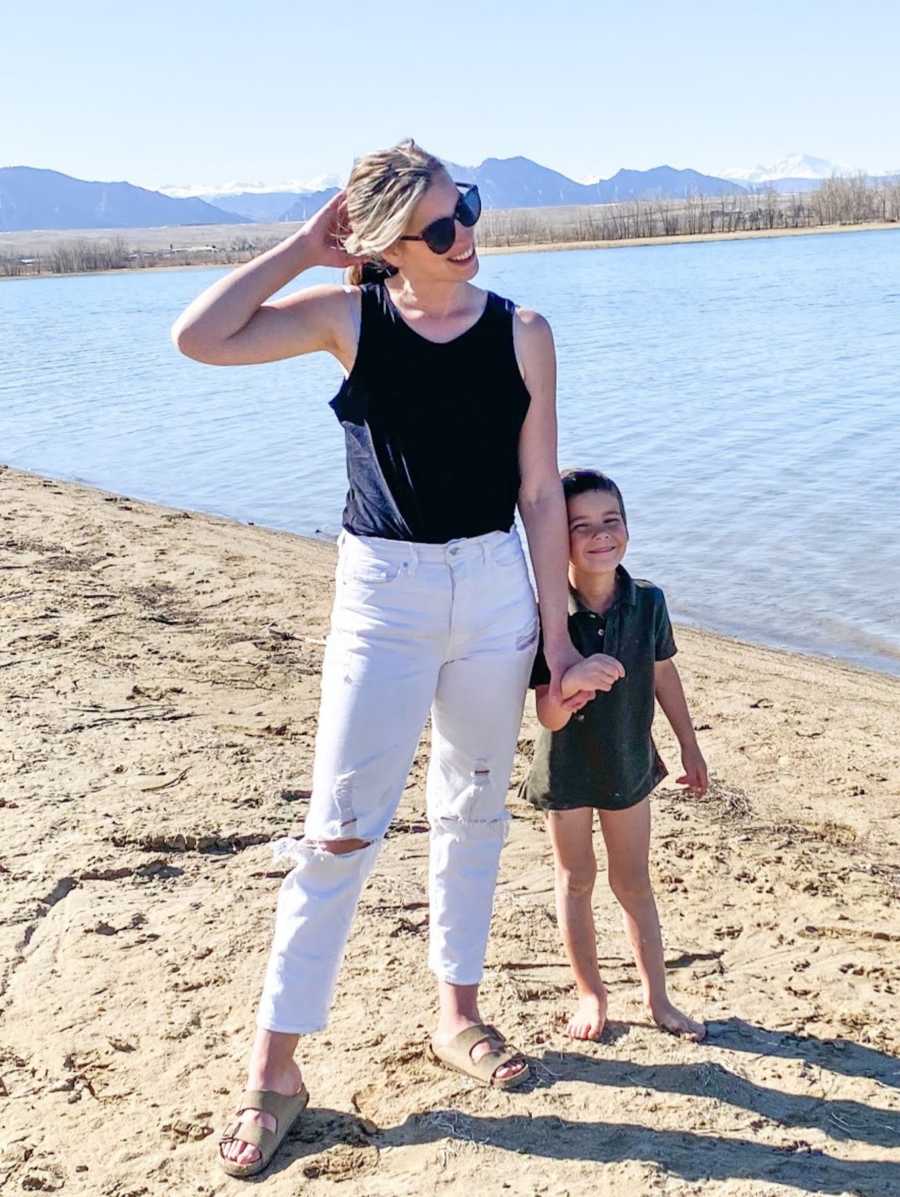 Teen mom in white pants holds son on beach