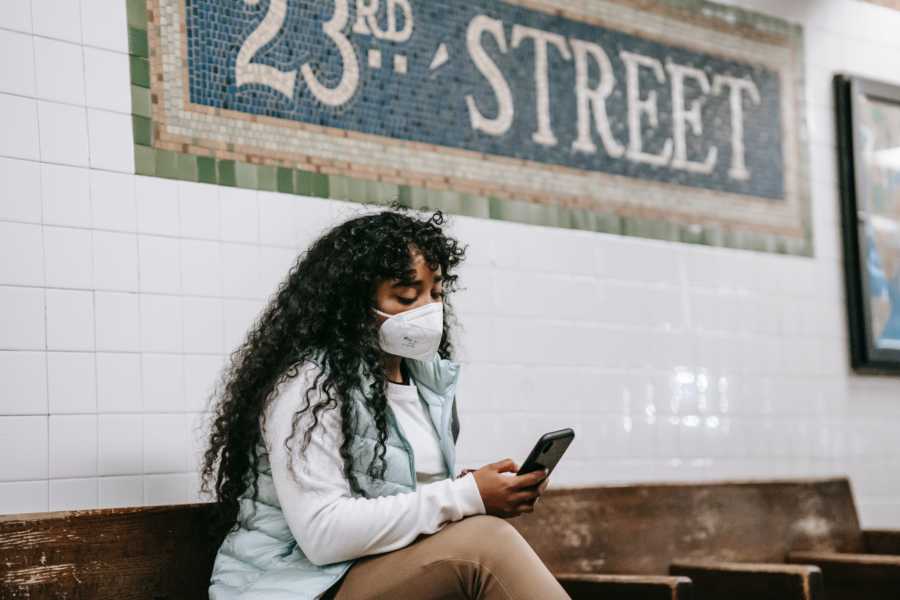 Woman with white face mask scrolls through phone on subway platform