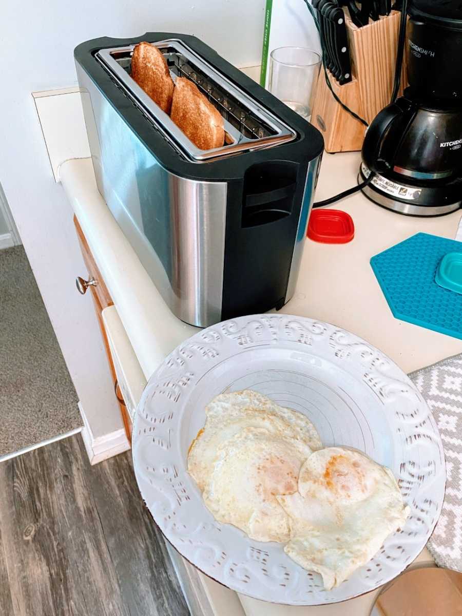 A mom shows off her breakfast of two fried eggs on a plate and two pieces of toast, still in the toaster