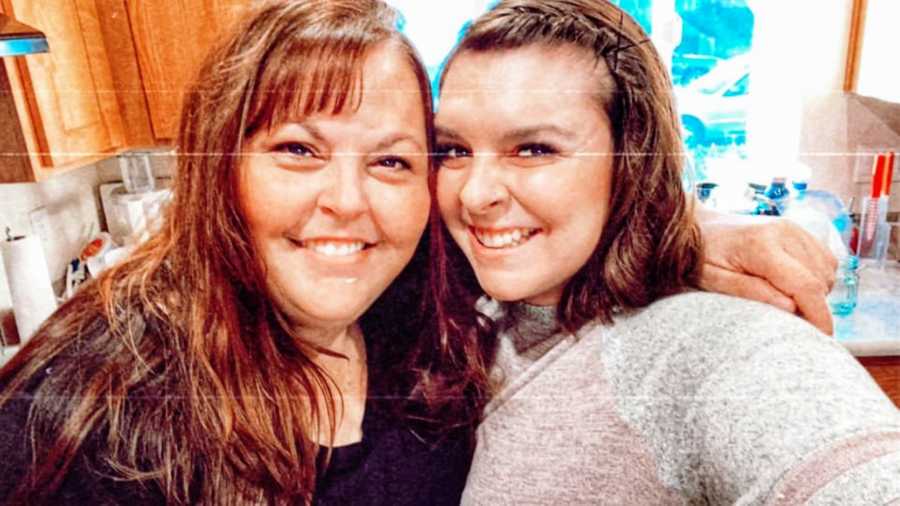 Woman smiles and takes selfie with mom in kitchen