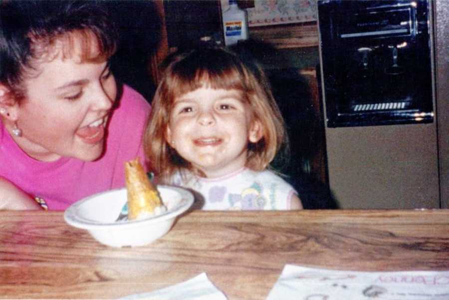 Young girl smiles at camera while eating ice cream with her mother