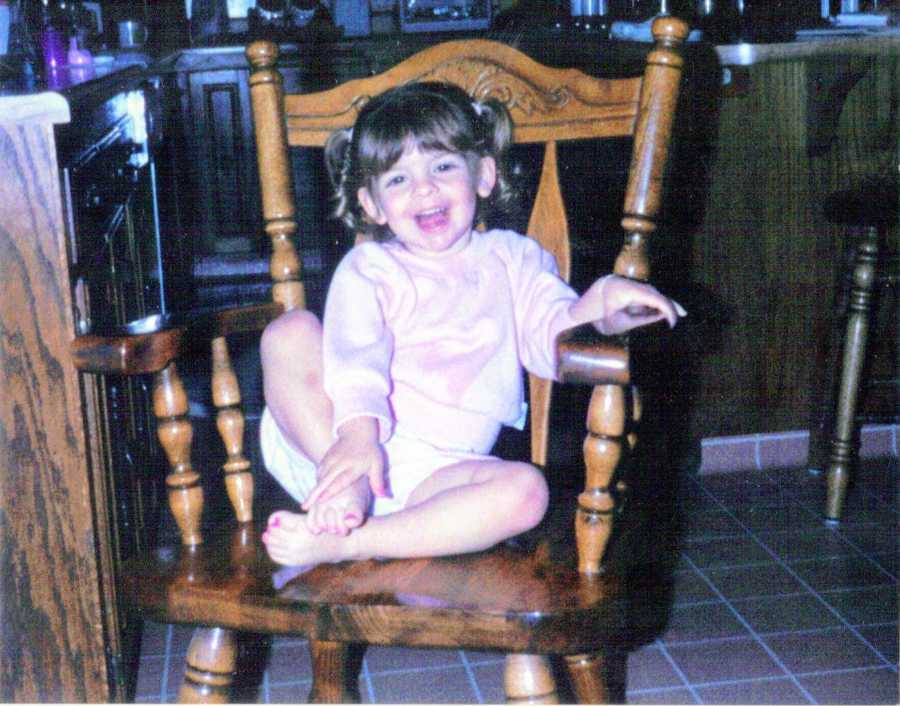 Young girl with pigtails smiles at camera while sitting in wooden chair