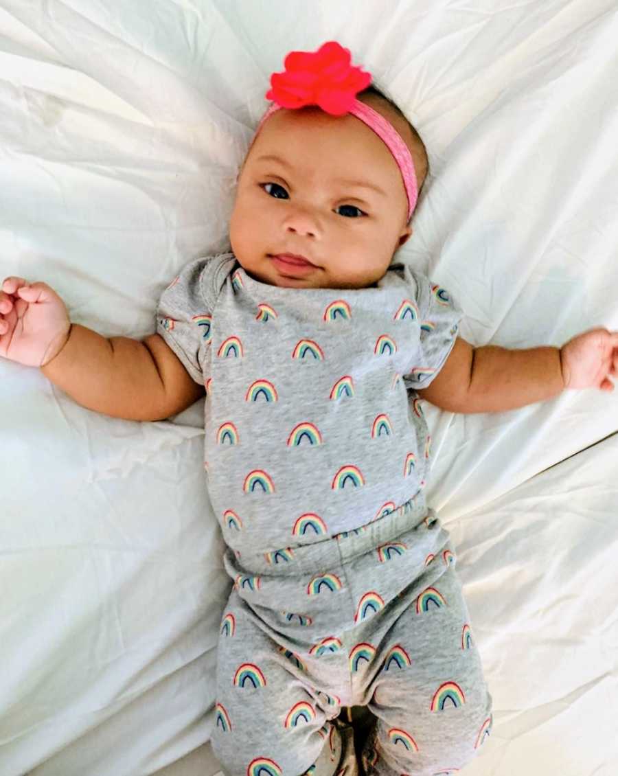 Newborn baby lying on white blanket wearing onesie with rainbows