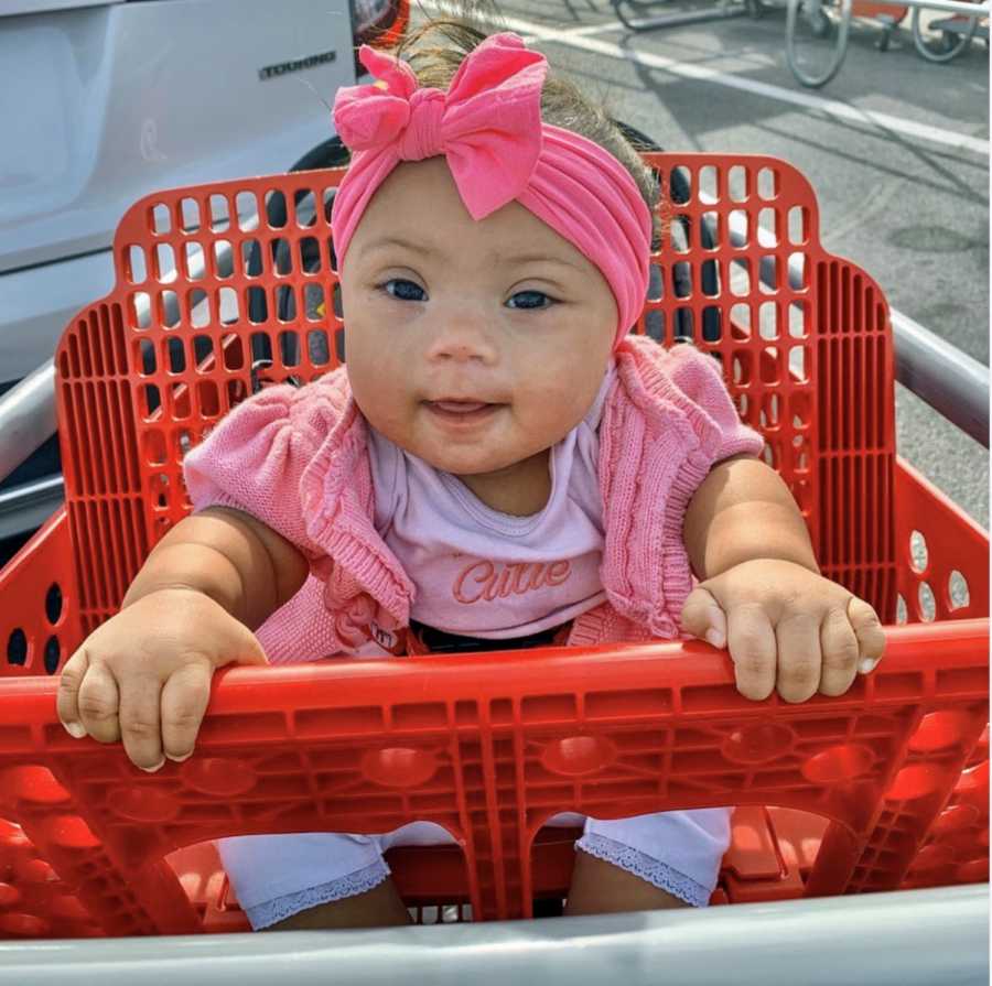 Baby girl wearing pink sitting in red grocery cart