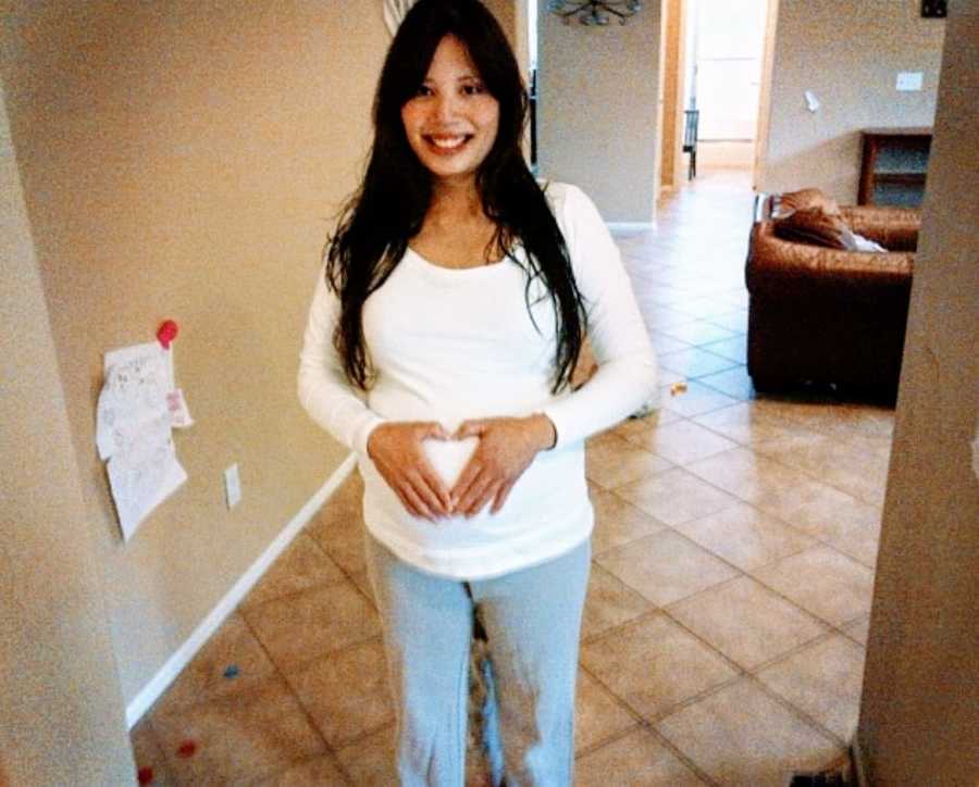 Woman pregnant with a baby girl poses for a photo while making a heart over her belly with her hands