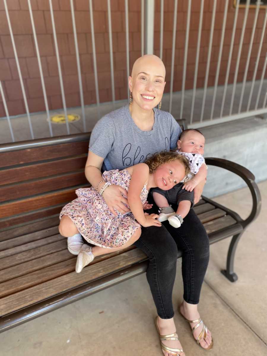 woman holding her two children on a bench