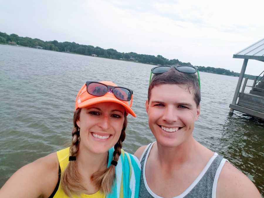 Couple smile and take a selfie in front of a lake in beach wear