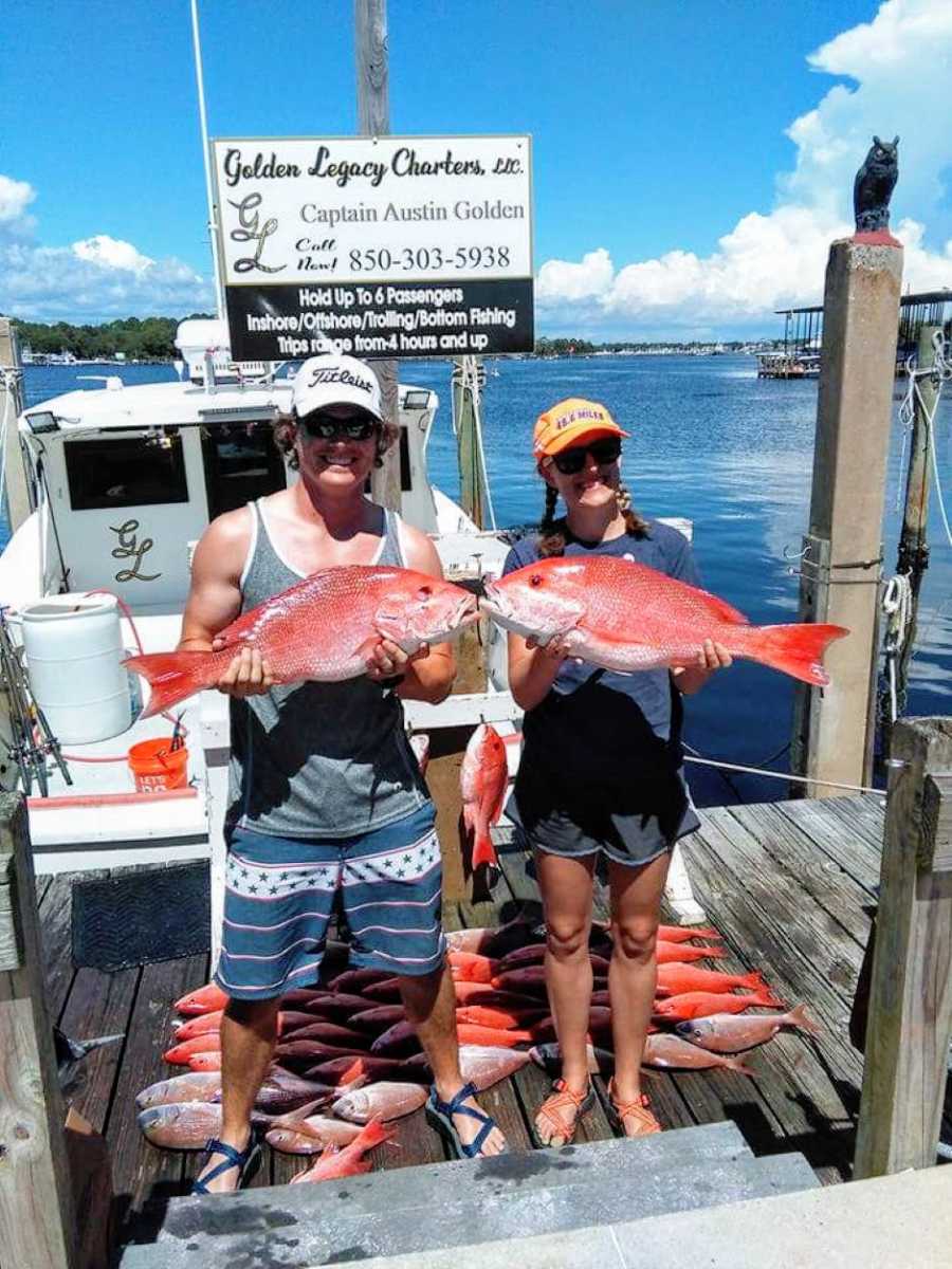 Couple out on a dock smile and hold up Red Snapper with the rest of their catches behind them
