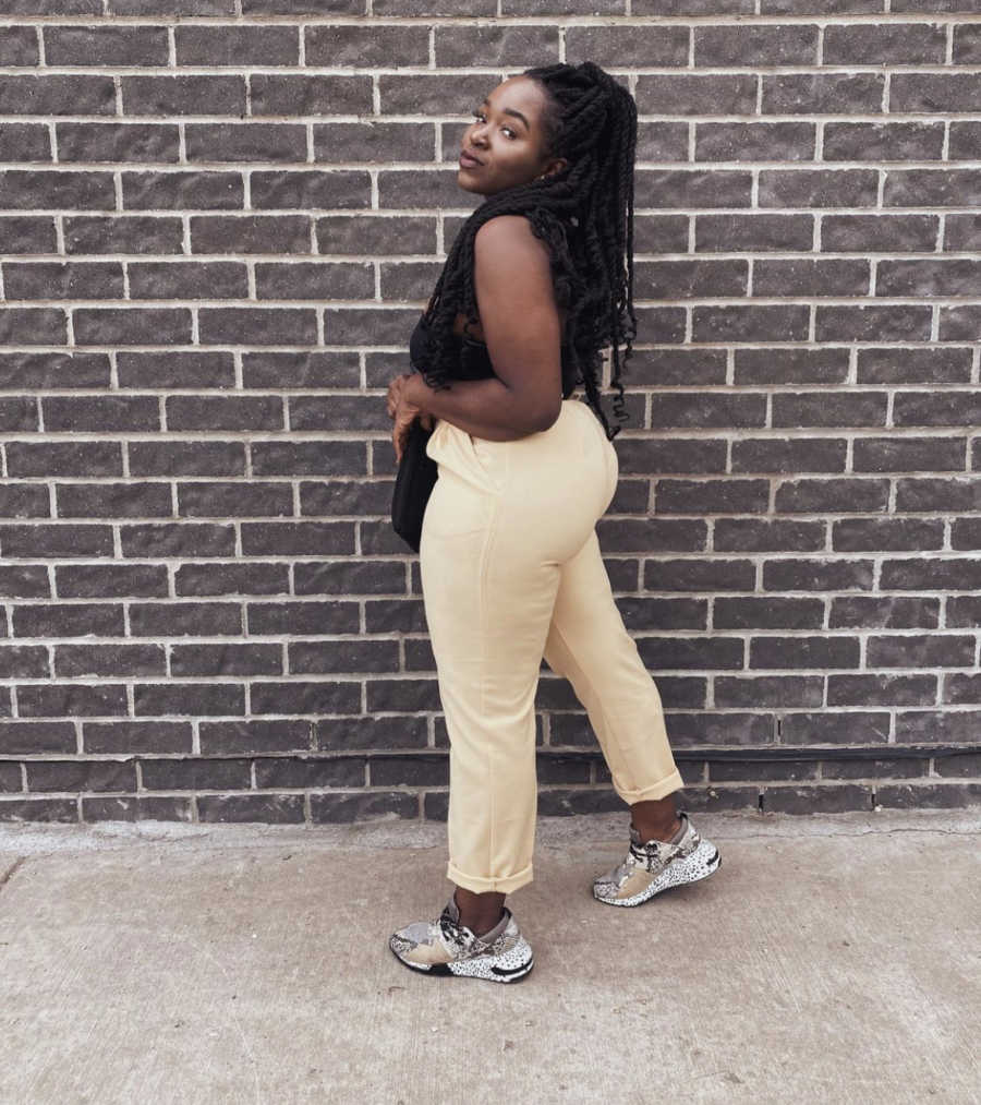 Body positive black woman poses in front of a brick wall.