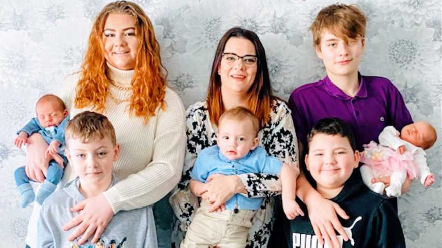 Mom poses for a photo with her seven children, with her two oldest standing on either side of her and each holding her newborn twins