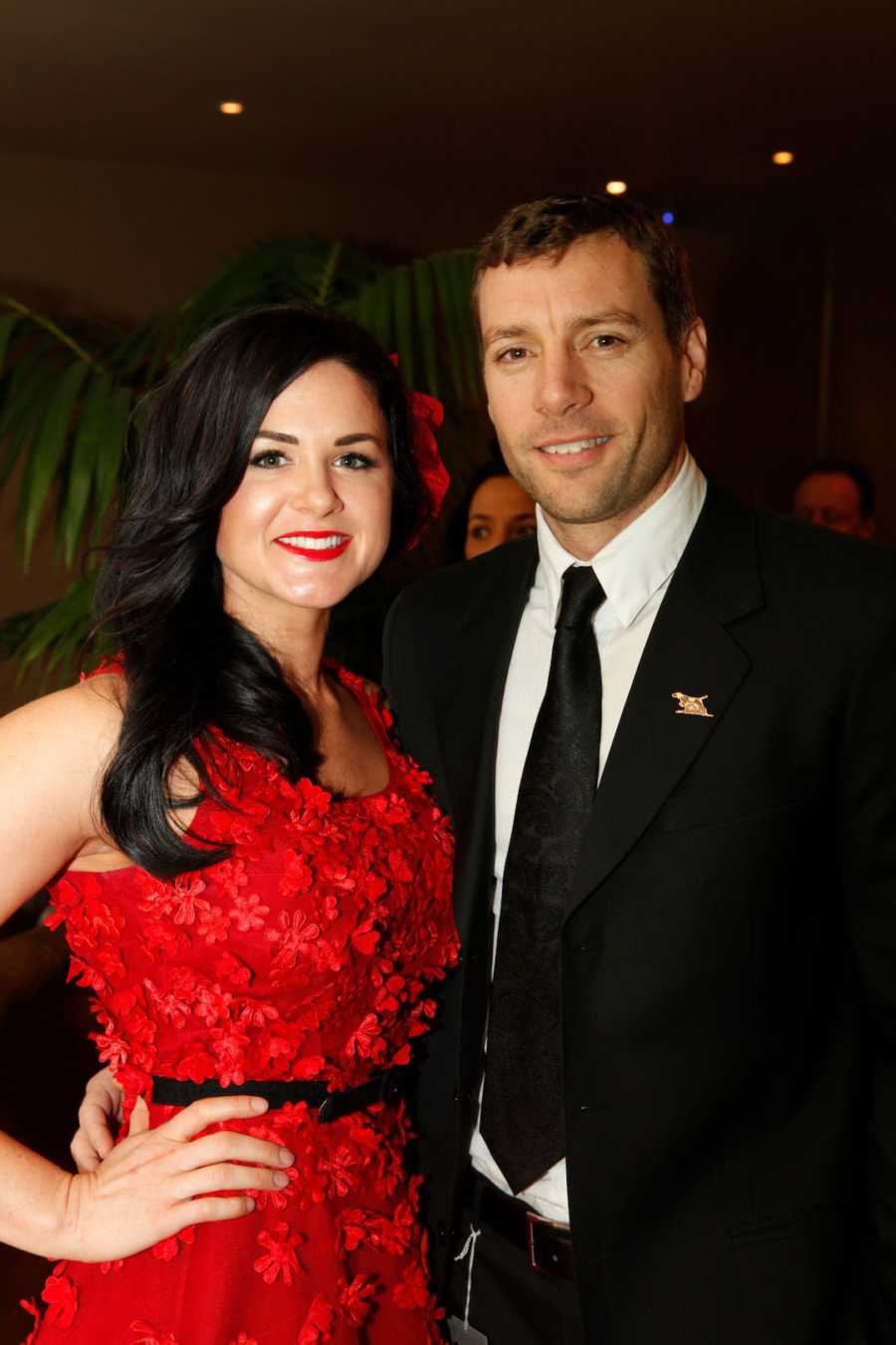 Husband and wife wearing red dress smiling together