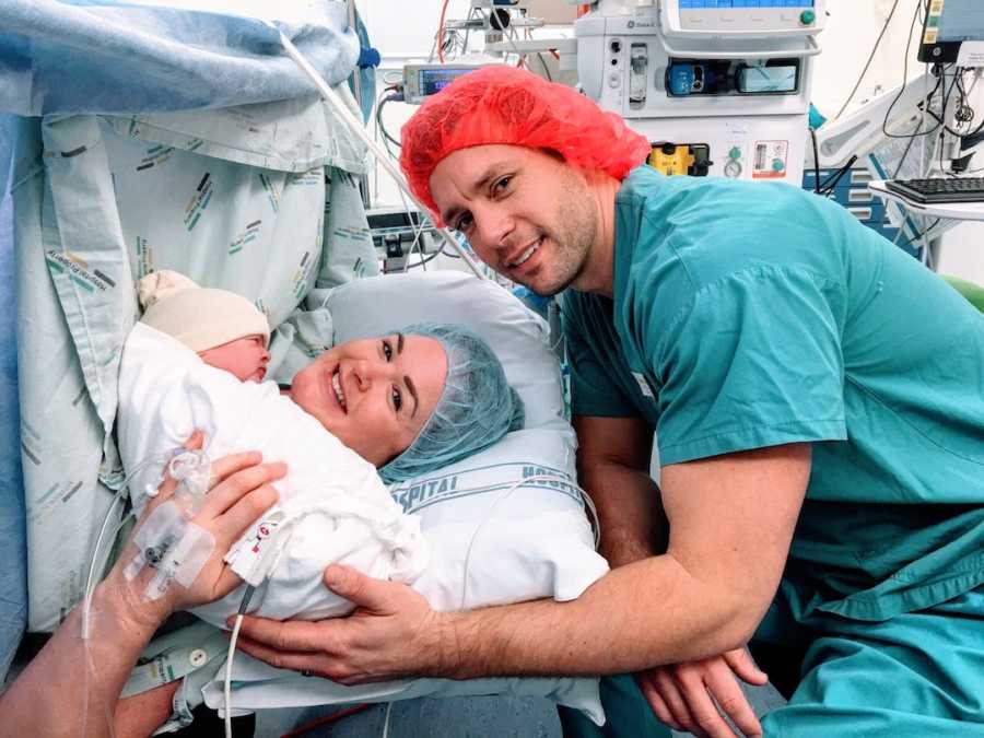 Husband and wife in hospital holding their newborn baby wearing scrubs
