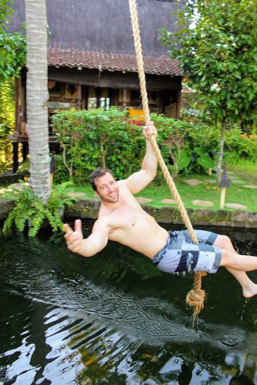 Man swinging on rope above body of water