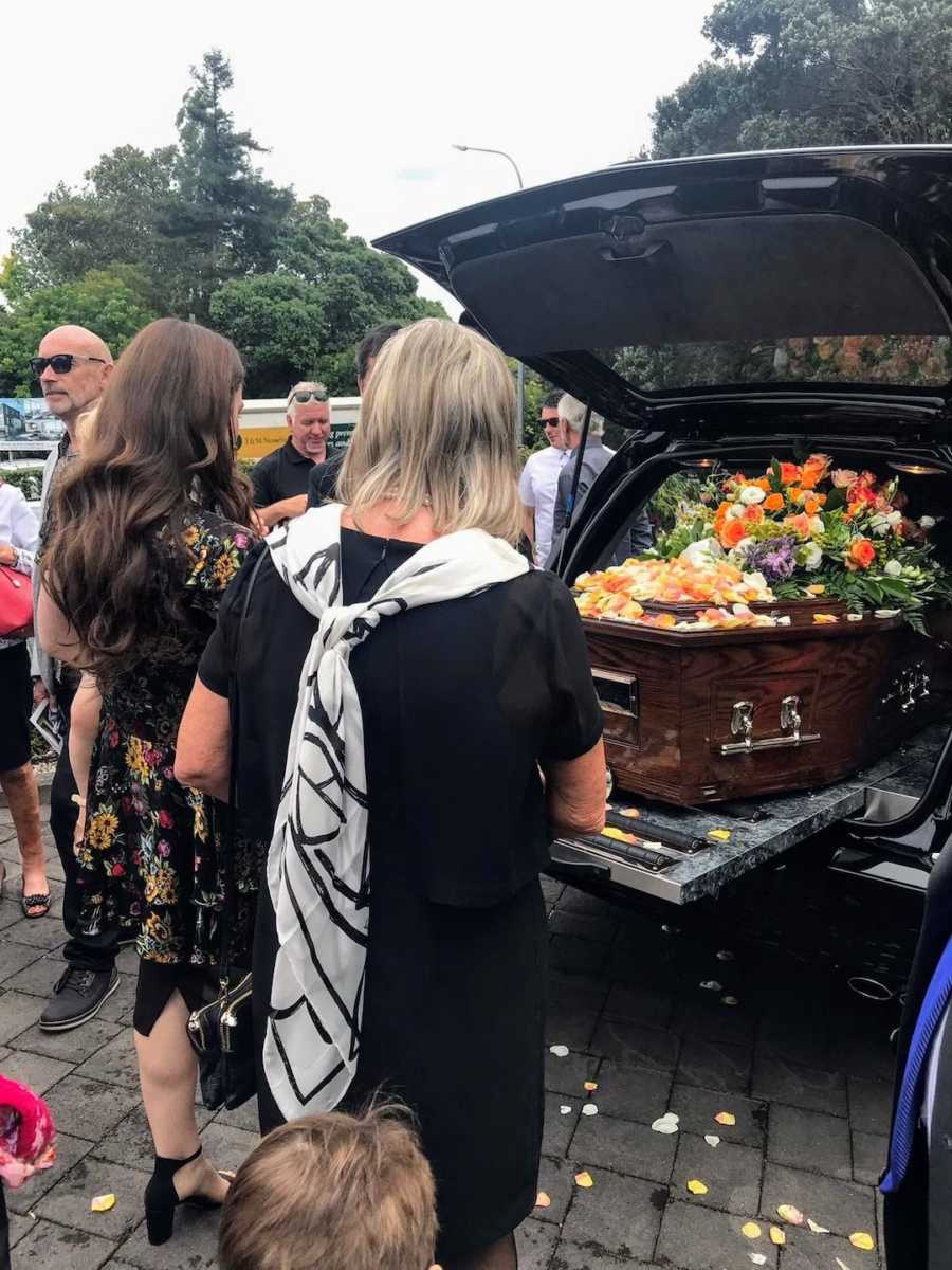 Two women standing in front of casket with flowers on it