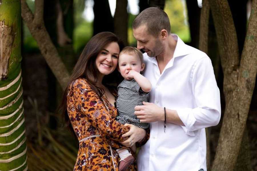 Husband and wife holding baby in front of trees