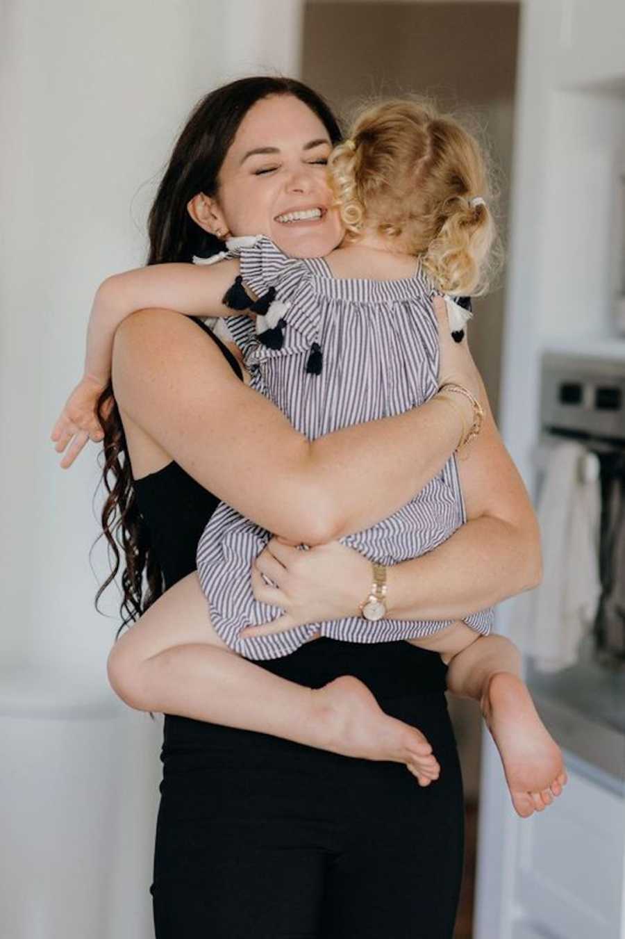 Mother wearing black hugging blonde daughter and smiling