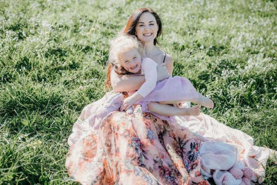 Mother wearing dress sitting with daughter smiling in grass