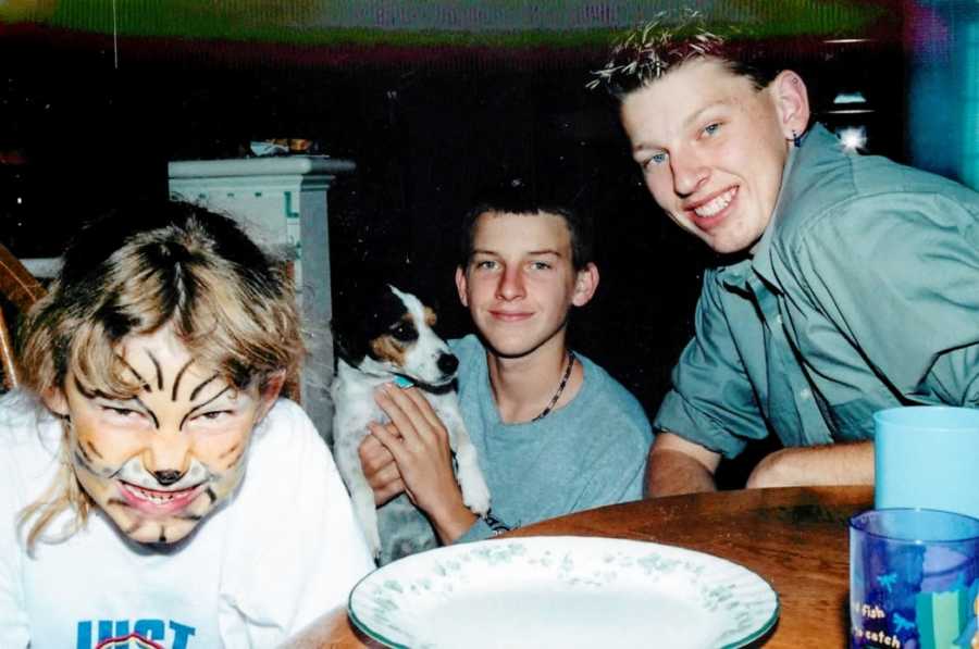 Young girl growls at the camera with tiger face paint on with her two brothers and family dog sitting beside her smiling